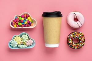 Cup of coffee, sweets and meringues in bowl in shape of cloud, chocolate with colorful topping and pink donut isolated on pink background Flat lay Top View Knolling Unhealthy and tasty food concept photo