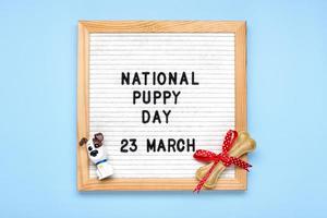 Felt board with text National puppy day in 23 march, cute dog figures, chewing bone with bow on blue background Top view Flat lay Holiday greeting card photo