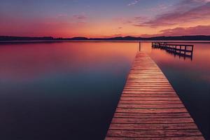 muelle de madera colorido en un lago que está totalmente tranquilo durante la puesta de sol foto