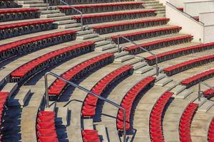 Empty red plastic chairs in the stands of the stadium or amphitheater. Many empty seats for spectators in the stands. photo