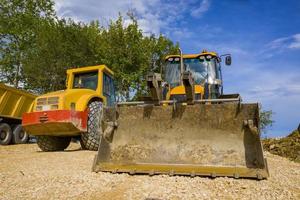 day view of yellow excavator with a shovel and  single drum roller at the construction site photo