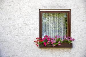 hermoso marco de ventana antiguo con caja de flores y pared gris claro. geranio o cranesbill en una caja de ventana. marco de ventana rural con espacio de copia. foto