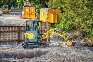 pequeña excavadora detenida con una pala y contenedores de construcción en el sitio de construcción foto