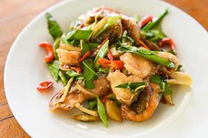 Comida tailandesa salteado de pescado con pimienta, ají y hierbas en la placa blanca - comida cocida de pescado tilapia foto