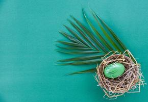Easter eggs in basket nest decoration with green palm leaves on green background photo