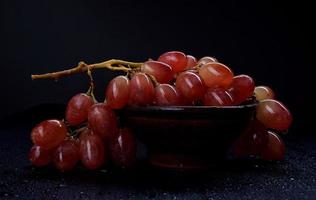 A bunch of ripe red grapes in a clay plate, on a dark background. photo