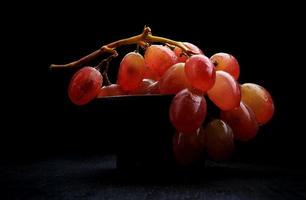 un racimo de uvas rojas maduras en un plato de arcilla, sobre un fondo oscuro. foto