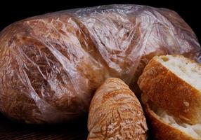 A loaf of bread wrapped in a plastic bag and slices of sliced bread nearby. photo