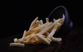 French fries in a clay cup and scattered nearby. French fries on a dark background. photo
