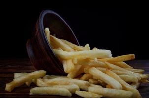 French fries in a clay cup and scattered nearby. French fries on a wooden table. photo