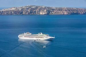 Cruise ship in the sea near the volcano of Santorini island, Greece. Beautiful tourism and travel background, transportation concept, summer vacation scenery. Sea transfer in Santorini photo