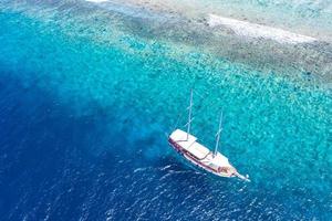 Aerial view of sailing boat anchoring on coral reef. Drone view, water sport theme. Luxury cruise and marine travel background. Beautiful nature scenery, sea ocean water concept. Maldives aerial