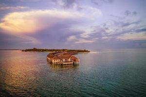 paisaje aéreo de puesta de sol en la isla de maldivas, resort de lujosas villas de agua y muelle de madera. hermosos colores de puesta de sol y fondo de playa para vacaciones de verano y concepto de viaje. paisaje aereo foto