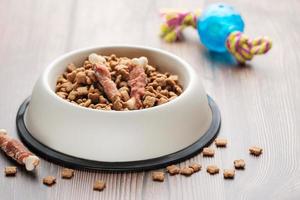 A bowl with dog food, dog treats and toys on a wooden floor. photo