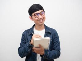 Positive man jeans shirt wearing  glasses writing on diary looking up photo