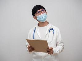 Doctor wearing medical mask hold check list board looking above white background photo