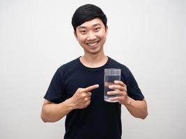 un alegre hombre asiático señala con el dedo un vaso de agua de fondo blanco foto