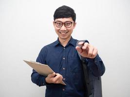 Cheerful man wearing glasses holding clipboard with backpak point pen at you photo