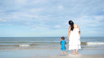 madre e hijo en la hermosa playa con olas marinas, vacaciones familiares en el paisaje oceánico foto