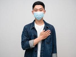 Positive man jeans shirt wear medical mask touching his chest gentle smile isolated photo