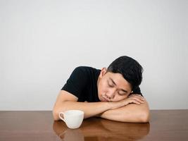 hombre insomne sentado a dormir en la mesa con una taza de café por la mañana foto