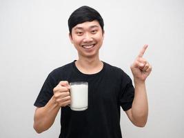 Man smiling and holding glass of milk point finger at copy space photo
