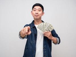 camisa de jeans de hombre guapo sostenga el dólar de dinero y señale con el dedo foto