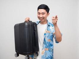 Cheerful man beach shirt hold luggage smiling point finger at you photo