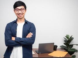 hombre de negocios positivo gafas sonrisa stand brazos cruzados en el espacio de copia de la sala de trabajo foto