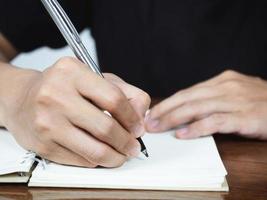 Close up man hand writing pen on book page on table photo