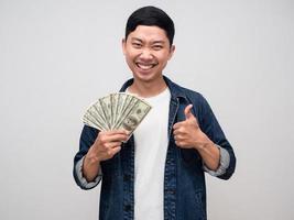 Cheerful asian man jeans shirt gentle smile earn money in hand and thumb up isolated photo