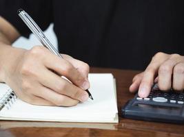 cerrar la pluma de escritura a mano para la contabilidad en el portátil con el uso de la calculadora foto