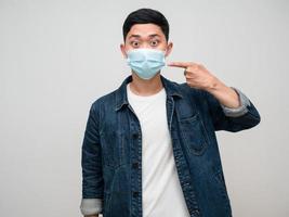 Positive man jeans shirt wearing medical mask point finger at his mask isolated photo