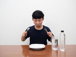 Young man holding cutlery looking at empty dish on the table with water on table photo