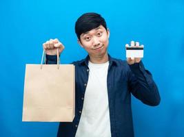 Portrait positive man holding paper bag and credit card for shopping blue background photo