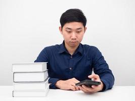 el hombre se sienta a la mesa con libros usando el teléfono móvil foto