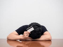 Depressed man laying head down on table hold credit card strain with debt about crisis photo