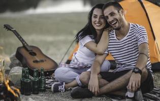 concepto de vacaciones de picnic. hermosa pareja divirtiéndose haciendo barbacoa en la hoguera y relajándose junto a un lago. foto