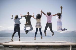 Portrait of young friends jumping from jetty into lake. Friends in mid air on a sunny day at the lake. photo