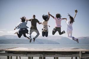 Portrait of young friends jumping from jetty into lake. Friends in mid air on a sunny day at the lake. photo