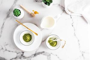 Green natural matcha tea powder in white ceramic bowls to prepare a healthy drink. top view. marble background. photo