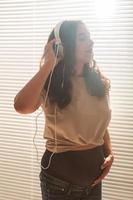 Curly-haired brunette pacified pregnant woman listens to pleasant classical music using smartphone and headphones. Concept of a soothing mood before meeting baby. photo
