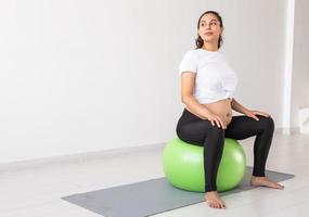 A young pregnant woman doing relaxation exercise using a fitness ball while sitting on a mat. Copyspace photo