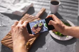 Hands take pictures on smartphone of two beautiful healthy sour cream and avocado sandwiches lying on board on the table. Social media and food concept photo