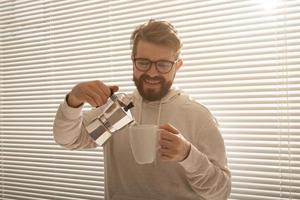 Young man pouring coffee from moka pot at morning. Breakfast and break concept. photo