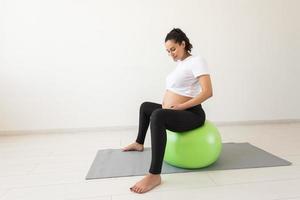 beautiful young pregnant woman doing exercise at home on fitball photo