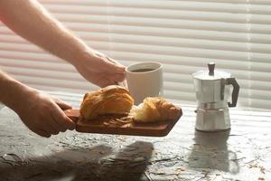 Breakfast with croissant on cutting board and black coffee. Morning meal and breakfast concept. photo