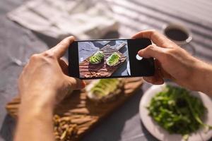 Hands take pictures on smartphone of two beautiful healthy sour cream and avocado sandwiches lying on board on the table. Social media and food concept photo