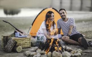 concepto de vacaciones de picnic. hermosa pareja divirtiéndose haciendo barbacoa en la hoguera y relajándose junto a un lago. foto