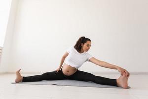 una mujer embarazada decidida hace ejercicio durante la clase de yoga y se relaja mientras se sienta en una alfombra en el suelo. concepto de preparación física y mental del cuerpo para el parto. lugar para texto foto